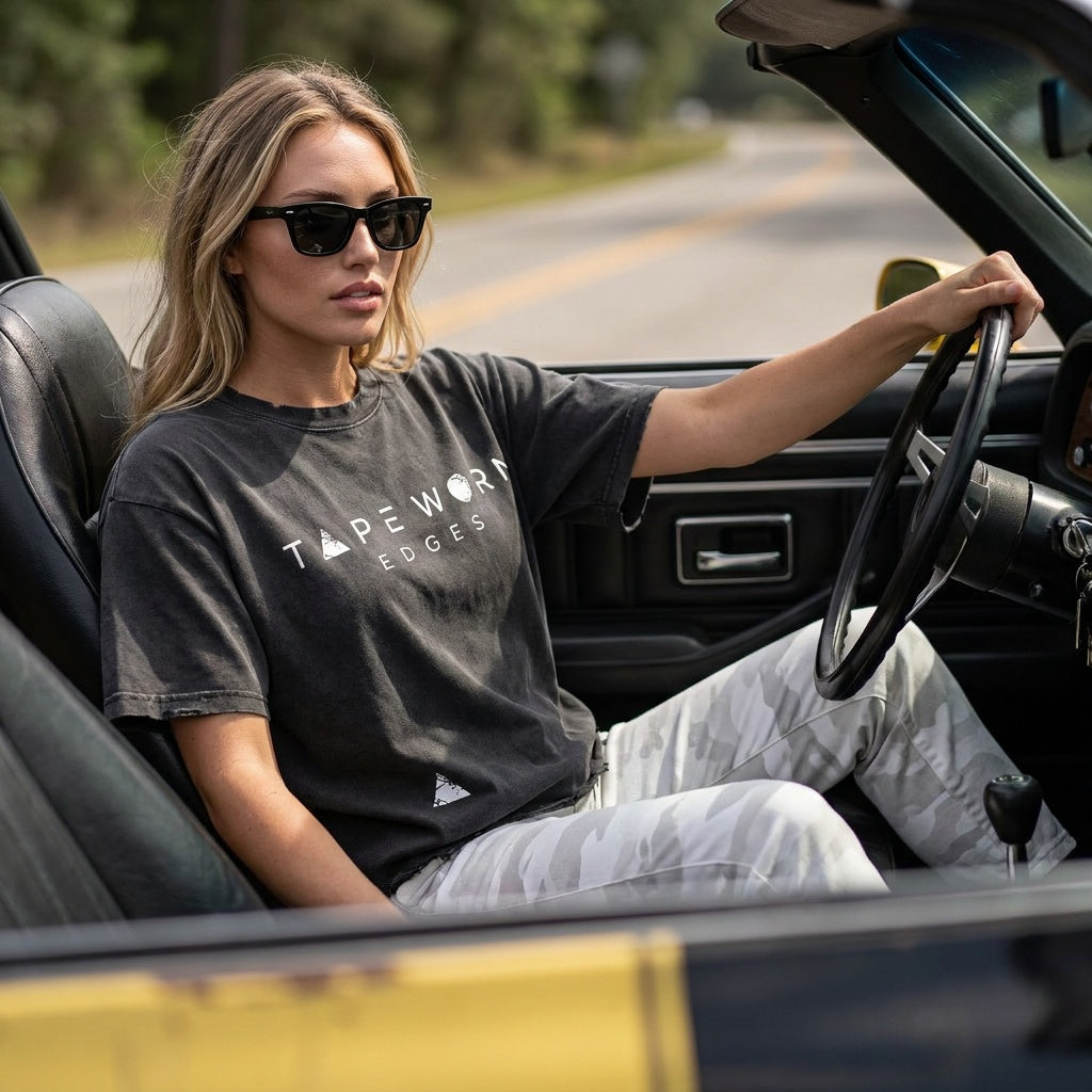 still, the product turned toward the camera, shallow depth of field — driving a convertible 1977 Chevrolet Camaro (yellow, black stripes, worn condition)